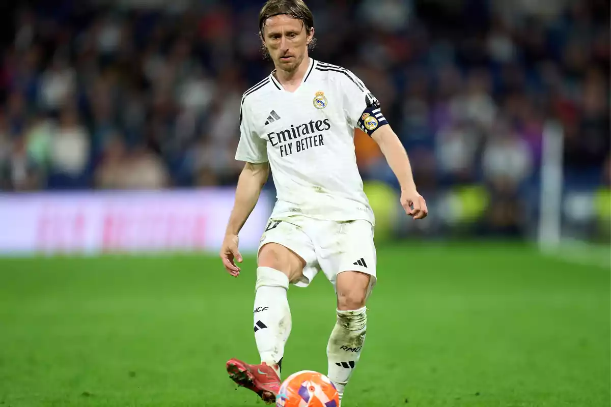 Un jugador de fútbol con uniforme blanco controla el balón en el campo durante un partido. Un jugador de fútbol con uniforme blanco controla el balón en el campo durante un partido.